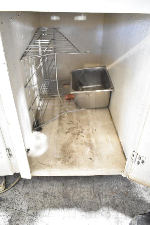 Commercial citrus juicer cabinet interior, housing space with metal racks and a removable stainless steel bin. Model details not visible.