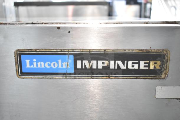 Lincoln Impinger commercial conveyor pizza oven label, visible wear on metal surface, on equipment stand.
