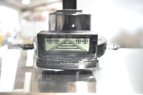 Black digital display with geometric symbols, mounted on shiny metallic surface. Part of an industrial equipment assembly.