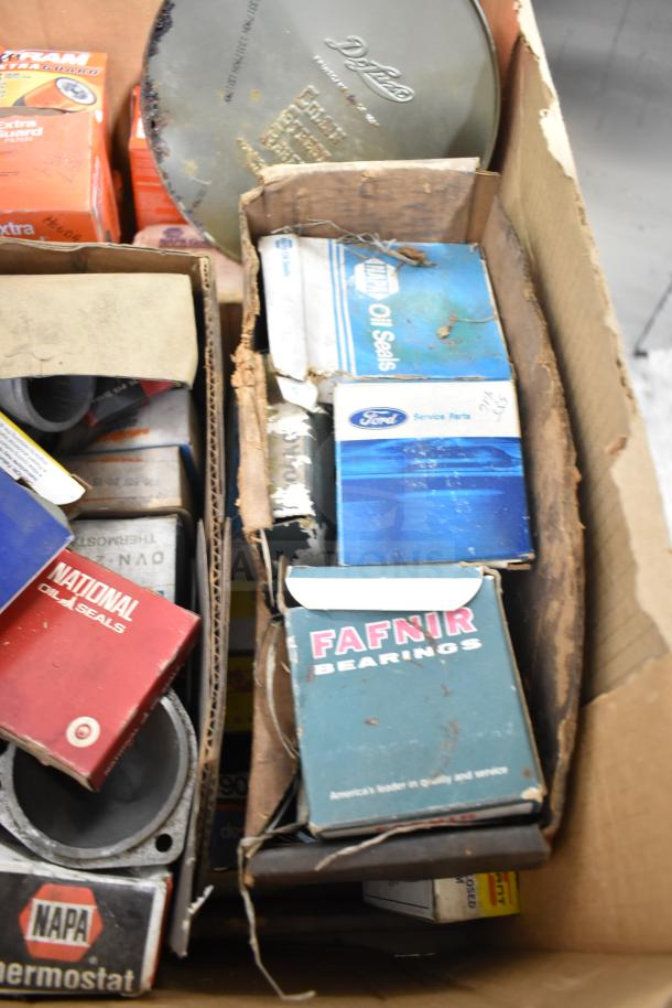 Lot of automotive parts including Fram PH4967 Extra Guard, Napa thermostat, Ford service parts, visible boxes with wear.