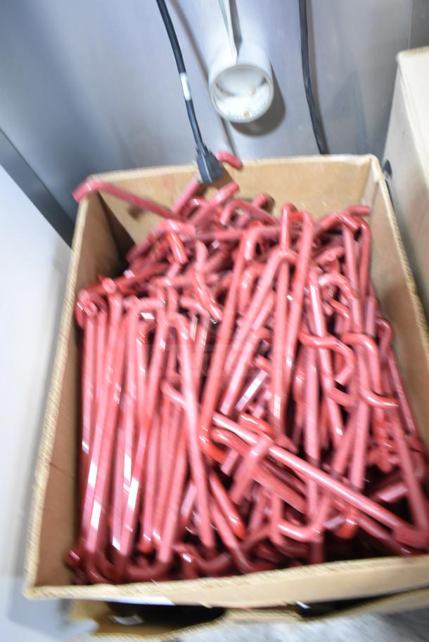 Lot of 4 boxes containing red metal hooks in a cardboard box. Hooks are shiny and slightly curved, ideal for industrial use.