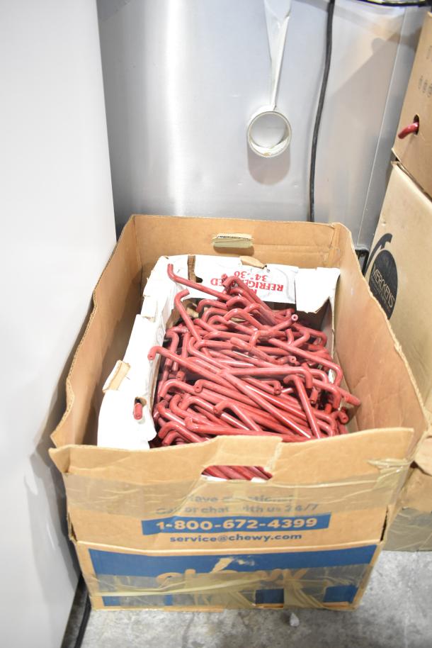 Cardboard box filled with red metal hooks, some attached to cardboard inserts. Box shows signs of wear.