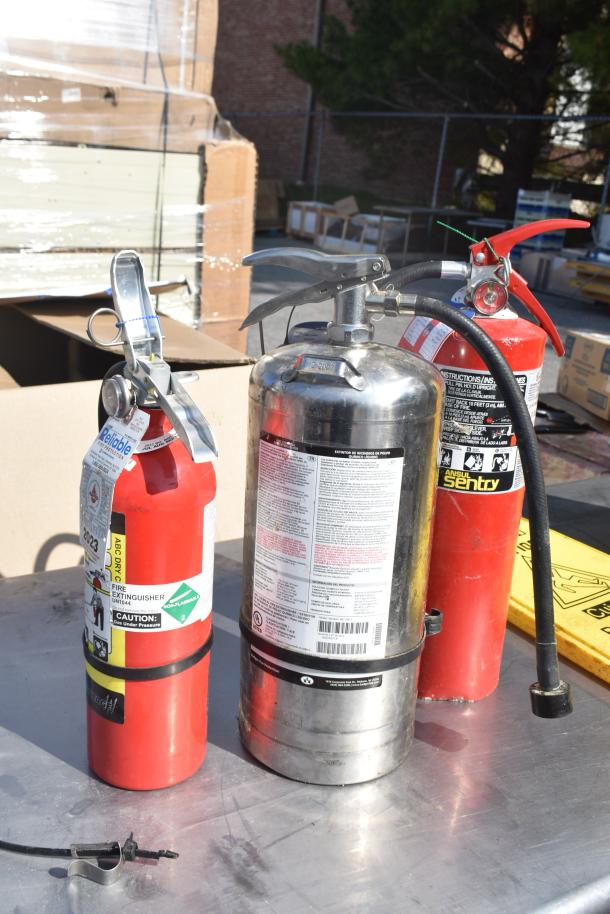 Commercial table with contents including three fire extinguishers and a yellow dolly on top. Labels visible.
