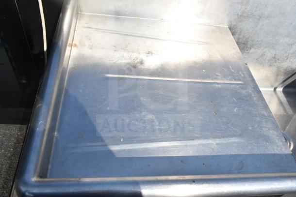 Commercial two-bay stainless steel sink with dual drain boards, showing slight wear. Ideal for heavy-duty kitchen use.