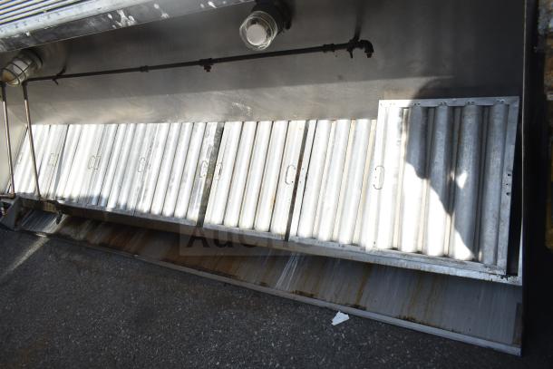 9' commercial grease hood with filters and overhead lights. Made of stainless steel, minor wear visible, industrial-grade.
