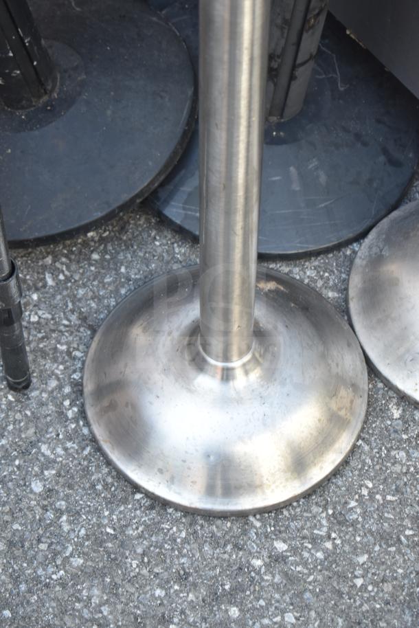 Six stainless steel stanchions with sturdy bases shown. Includes scuff marks and surface wear, ideal for crowd control.
