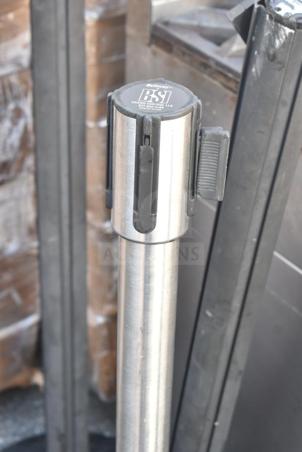 BSI stanchion with retractable belt, metallic finish, used for crowd control. Logo on top: "Beltway BSI Crowd Control LLC."