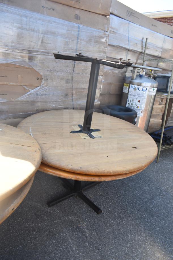 Four round wooden tables, one missing a base. Slight wear visible. Black metal legs on the remaining bases. 
