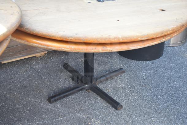 Four round wooden tables, one missing a base, showing wear and scratches, outdoor setting, ready for auction.
