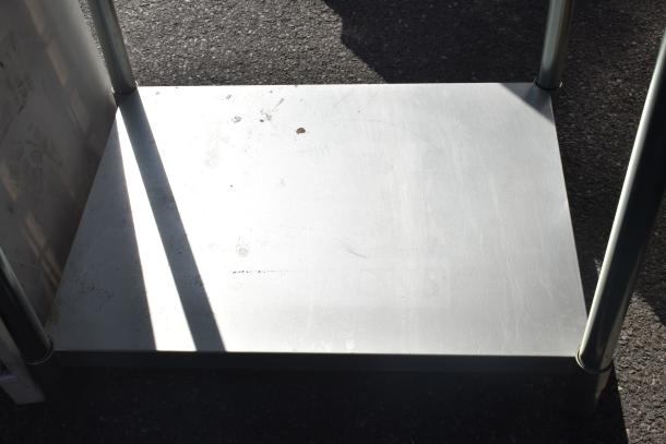 Commercial table with under shelf, metal construction, visible scratches and wear, sturdy legs, suitable for heavy-duty use.