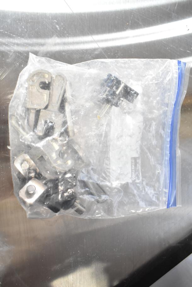 Plastic bag containing metal screws and hardware for Oliver 797-32NC bread slicer, displayed on a metal surface.