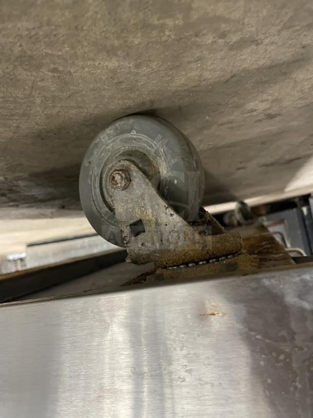 Caster on a commercial stainless steel countertop griddle/broiler, US Range model PX-6-24BG-2626. Visible wear.