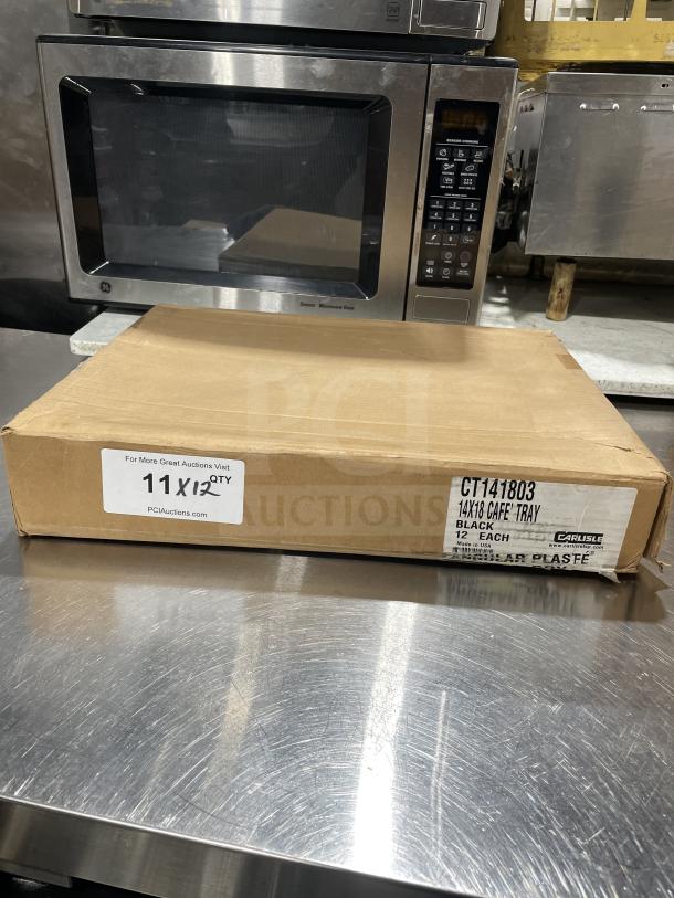 Brown box containing Carlisle NCT1418 black 14"x18" serving trays, new condition, labeled for auction, 12 per package.