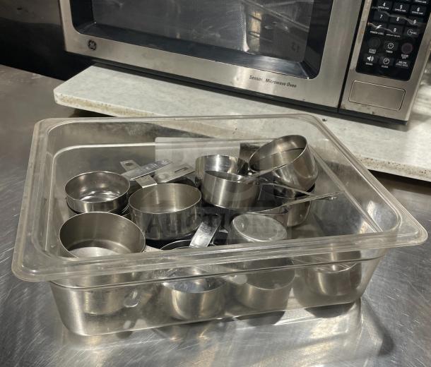 Commercial stainless steel measuring cups set in clear container, good condition, durable for kitchen use.