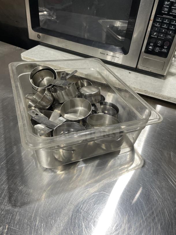 Commercial stainless steel measuring cups set in clear plastic container, excellent condition, ideal for precise measurements.