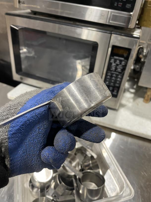 Commercial stainless steel measuring cups, durable with ergonomic handles, shown in a plastic container. Suitable for professional kitchens.