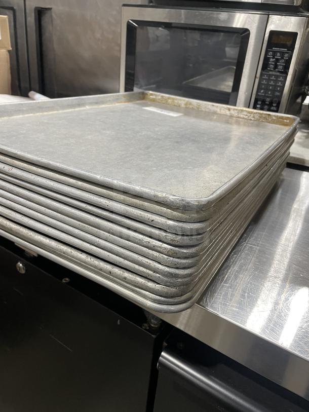 Stack of stainless steel Focus Food Service baking sheets, used condition, shown in a commercial kitchen setting.