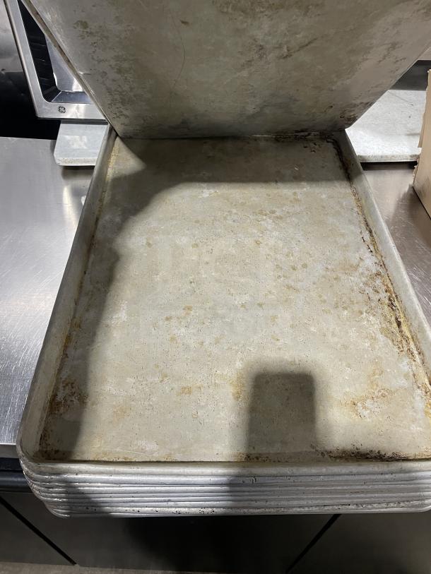 Stainless steel Focus Food Service baking sheets, stack of multiple pans, showing wear. Auction bid multiplies by 11.