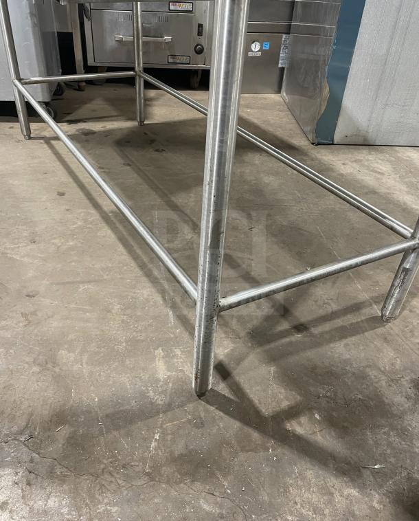 Stainless steel work/prep table with sturdy frame. Slight wear visible, ideal for commercial kitchen use.