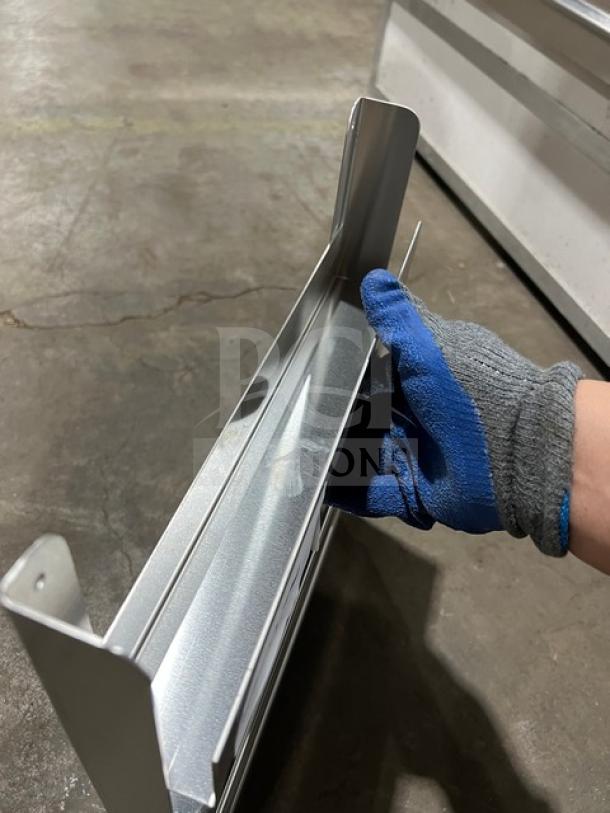 Stainless steel commercial side smoker/refrigeration rack, new, durable construction, close-up view with gloved hand.