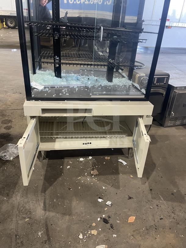 Commercial bakery display case, scratch and dent condition, glass front, metal shelving, under-storage space, visible damage.