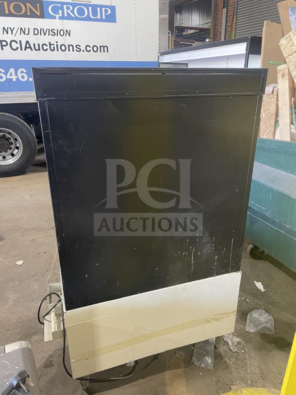 Commercial bakery display case with scratches and dents, black exterior, power cord visible, suitable for showcasing baked goods.