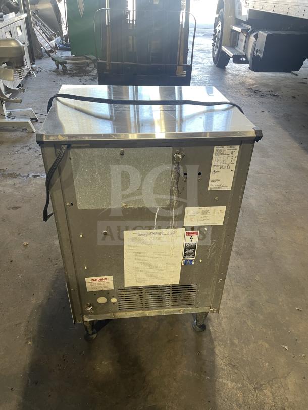 Ice O-Matic commercial ice maker, model ICEU220HA3, on legs. Features visible wear, labels intact showing specs and warning.
