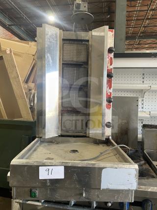 Commercial gas-powered vertical broiler with four burners, stainless steel construction, visible wear, and model number tag.