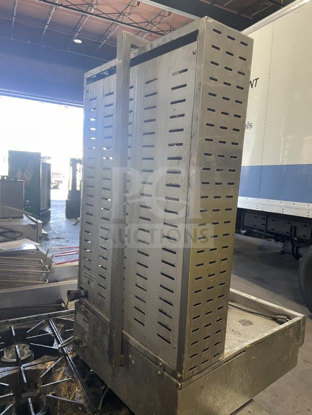 Commercial gas-powered vertical broiler with 4 burners, stainless steel, used condition, industrial setting.