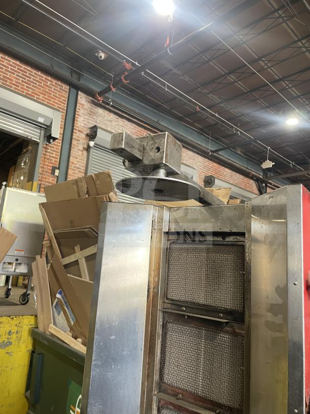 Commercial gas-powered vertical broiler with four burners, metallic finish, in a warehouse setting.