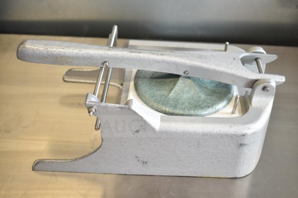 Industrial metal patty former with lever, cast structure, and turquoise base; shows wear, ideal for bulk food prep.