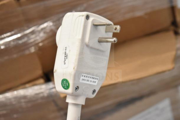 Power plug with visible markings including "0722301" and a "QC PASS" sticker, amid a blurred industrial background.