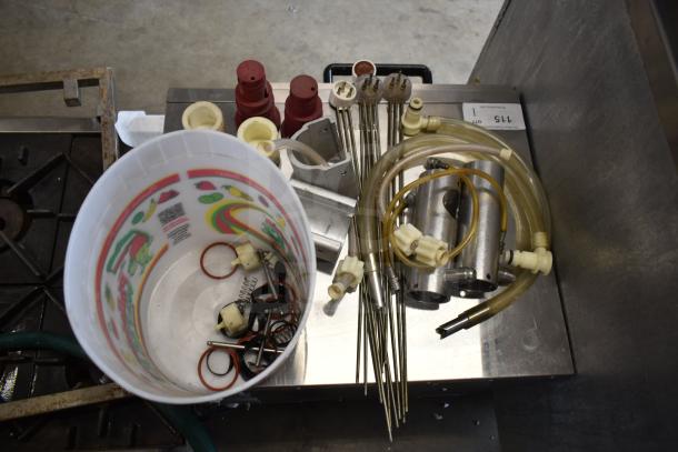92 various ice cream machine parts, including handles, hoses, and metal cylinders, in a mixed condition on a metallic surface.