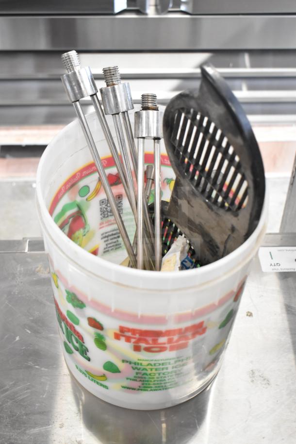 Bucket containing various ice cream machine parts, including metal handles and components. Visible label: "Premium Italian Ice."