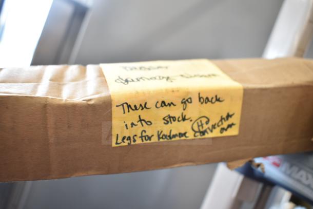 Cardboard box with yellow label reading, "These can go back into stock. Legs for KoolMore convection." Condition appears used.