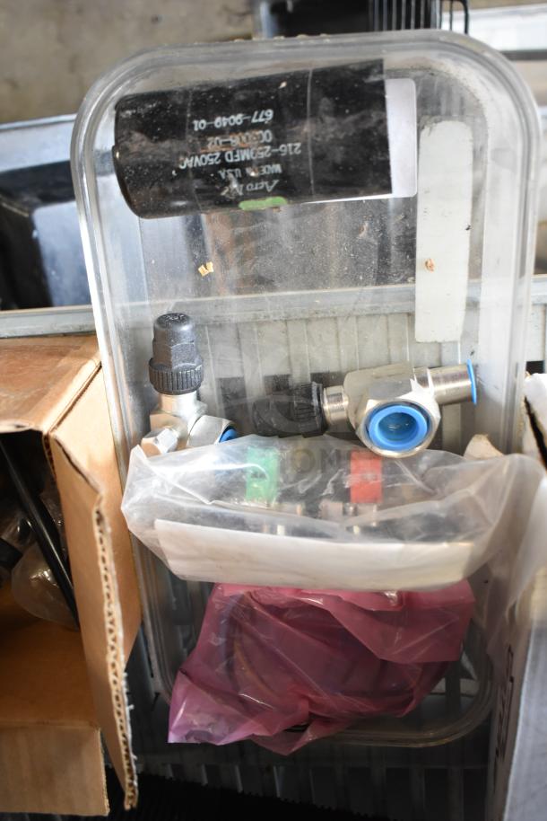 Assorted items including a drip tray, spigots, and mixing cup collars in a plastic container, showing various hardware.