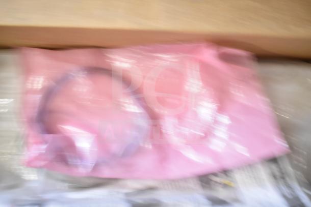 Blurry image of mixed auction items including range grates and Turbochef kick plates, wrapped in pink plastic.