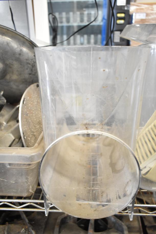 Assorted kitchen equipment including plastic beverage machine hoppers, metal meat grinder tray, and vegetable chute pusher, in used condition on metal shelves.