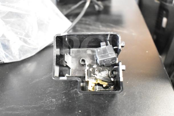 Box containing electronic components for a POS system, including switches and wiring, on a black surface.