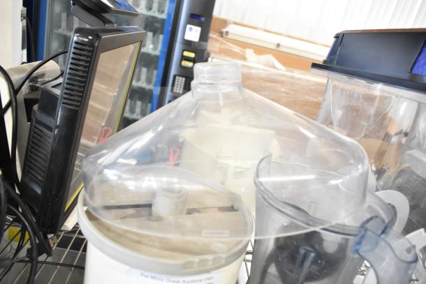 Assorted items, including slushie machine hoppers and blender pitcher, in lightly used condition on a metal shelf.