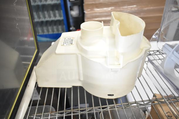 White slushie machine hopper on metal shelf, visible label with caution information. Other items partially visible.