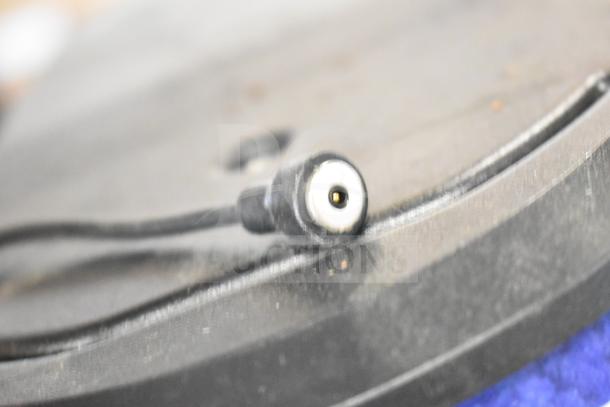Close-up of a black connector plug against a blurred background, part of a lot with slushie machine hoppers and other items.