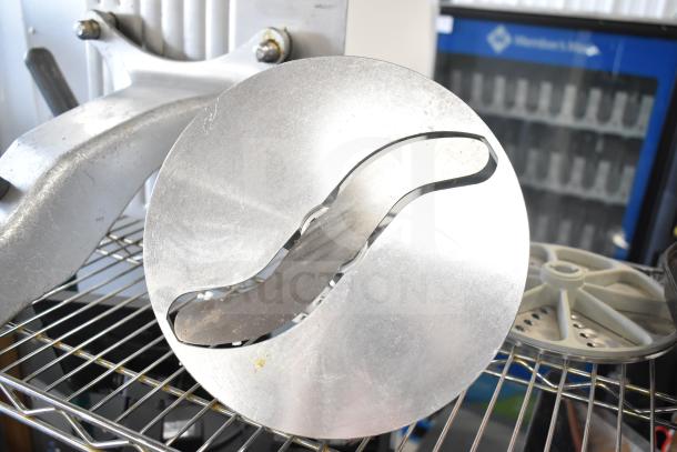 Various commercial kitchen blades, including a meat slicer arm and food processor blades, on metal shelving.