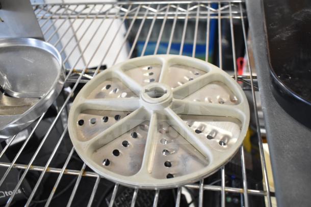 Metal food processor blade on wire rack, circular with perforated design, part of auction lot including slicer arm and pelican head blades.