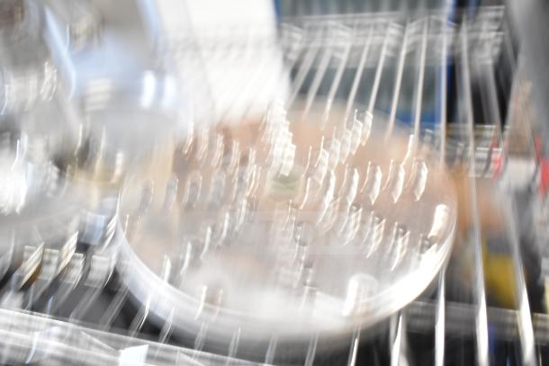 Blurred image of a metal disc with grooves, possibly a food processor blade, on a metal rack.