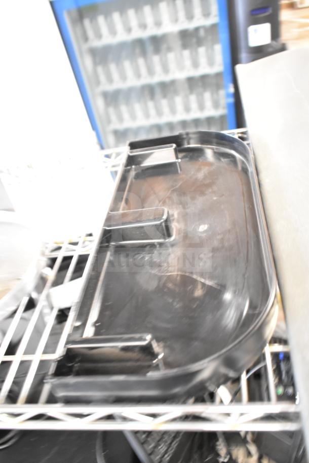Black plastic tray resting on a metal shelf, part of a lot including meat slicer arm and blades.