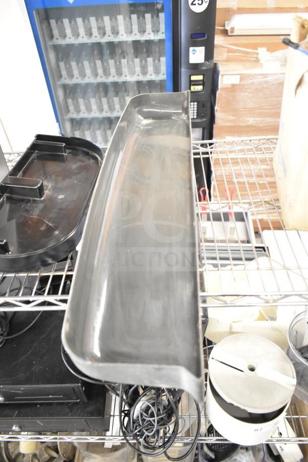 Metal meat slicer arm and various food processor blades on a storage rack. Assorted equipment includes cords and trays.