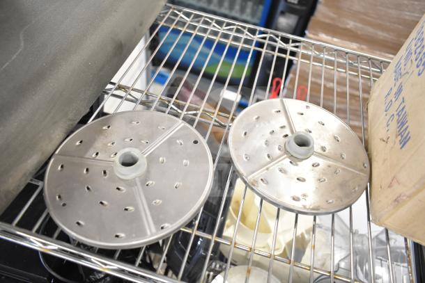 Metal food processor blades on a metal rack, showing perforated design for slicing, slight wear visible.