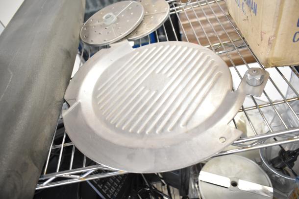 Various kitchen appliance components, including a meat slicer arm and pelican head blades, on a metal shelf.