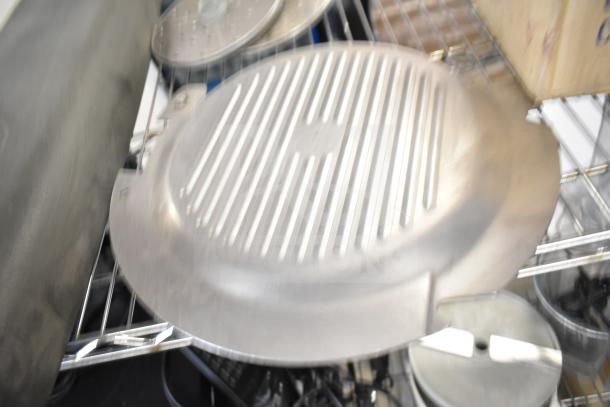 Metallic food processor accessory on wire shelf, includes a ribbed meat slicer arm and circular blades. Multi-item auction lot.